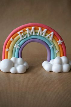 a rainbow cake topper sitting on top of a table next to white clouds and the word mama