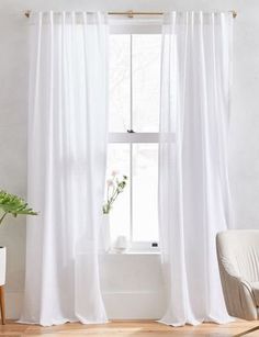 a living room with white curtains and a chair in front of a window that has a potted plant next to it