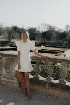 a woman in a white dress is standing on a balcony with her hands out and smiling