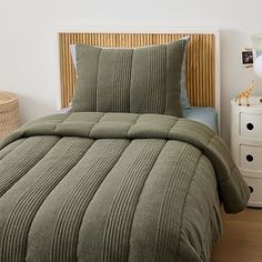 a bed with green comforter and pillows in a room next to a white dresser