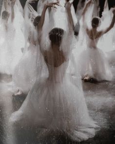 a group of women dressed in white dance under rain falling from their veils on the floor