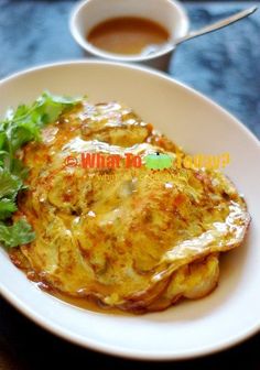 an omelet with lettuce and sauce on a white plate next to a cup of coffee