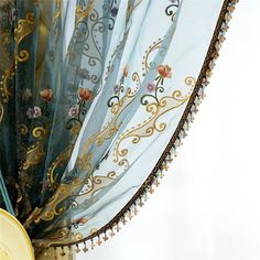 a close up of a curtain with flowers on it and tassels hanging from the side