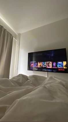 a flat screen tv mounted on the wall above a bed with white sheets and pillows