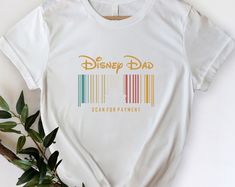 a white t - shirt with the word disney dad printed on it next to a plant