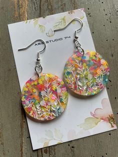 a pair of earrings with flowers painted on them sitting on top of a piece of paper