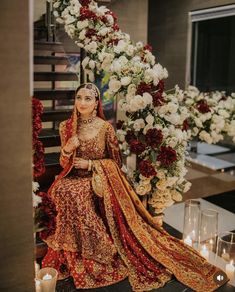 a woman in a red and gold wedding dress sitting on a table next to flowers