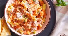 a plate of pasta with sauce and parmesan cheese on it next to bread