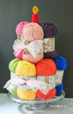 a stack of balls of yarn sitting on top of a glass cake plate with a lit candle