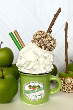 a green cup filled with whipped cream next to apples and cinnamon sticks on a table