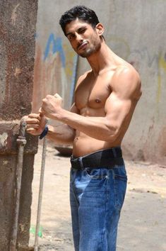 a shirtless man standing next to a pole with his hands on his hips and looking at the camera