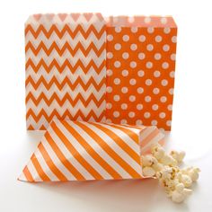 three orange and white paper bags with polka dots on them, one has popcorn in it