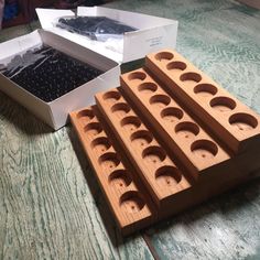 four wooden boxes with holes in them sitting on a table next to a box of beads