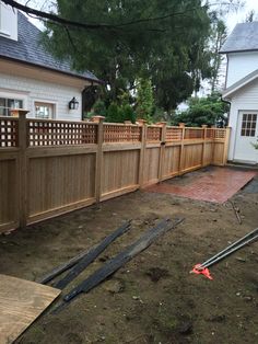 a wooden fence in front of a house with some tools laying on the ground next to it