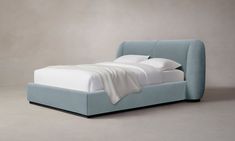 a blue bed with white sheets and pillows on it's headboard, sitting in front of a gray wall