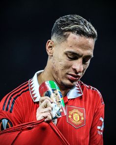 a man holding a cup in his right hand and wearing a red shirt with the manchester united crest on it