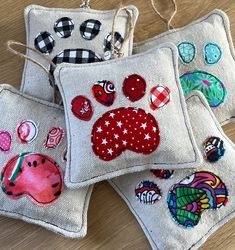 three embroidered pillows with designs on them sitting on a wooden table next to each other