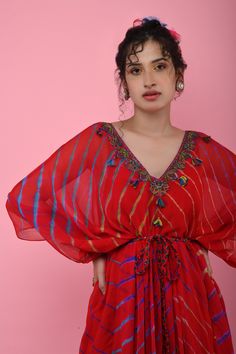 Red kaftan tunic with all-over multicolored Leheriya print, embroidered V-neckline and asymmetric hem. Comes with braided tie-up belt.
Component: 2
Printed, Embroidered
Neckline: V-Neck
Sleeve Length: Three Quarter
Fabric: Georgette
Color: Red
Asymmetric hem
Braided belt with tassels
Note: The inner slip and headscarf worn by the model is not for sale - Aza Fashions Summer Festive V-neck Kaftan, Designer V-neck Summer Dresses, Summer Designer V-neck Dresses, Designer Summer V-neck Dress, Multicolor V-neck Kurta For Eid, Bollywood Style V-neck Festive Kaftan, Bollywood Style V-neck Party Kaftan, Red V-neck Kurta For Festivals, Bohemian Designer Kaftan For Summer