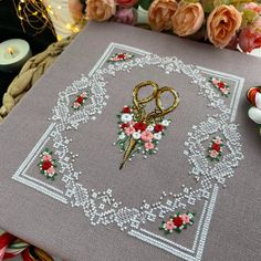 a pair of scissors sitting on top of a table next to some flowers and candles