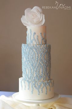 a white and blue wedding cake with a flower on top is sitting on a table