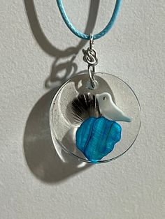 a glass pendant with a bird on it hanging from a blue cord necklace that is attached to a white wall