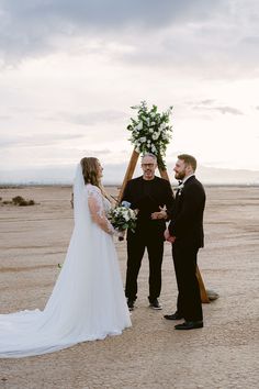 a man and woman standing next to each other in front of a wooden structure with flowers on it