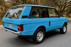 an old blue car parked on the side of the road in front of some trees