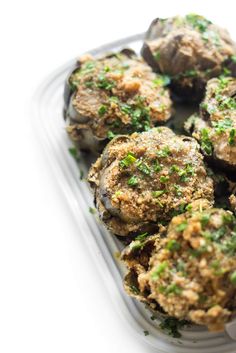 a plastic container filled with meatballs covered in parsley on top of a white table