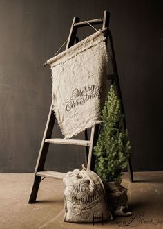 an old ladder with a christmas sack next to it and a small tree in front of it