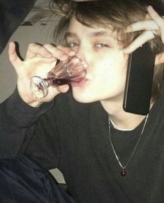 a young man drinking from a wine glass while holding a cell phone to his ear