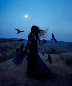 a woman standing on top of a dirt road next to birds flying in the air