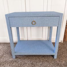 a small blue table on carpeted floor next to white wall and wicker basket