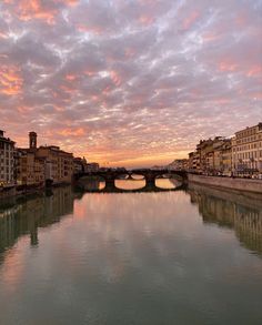 the sky is pink and purple as the sun sets over a river with buildings on both sides