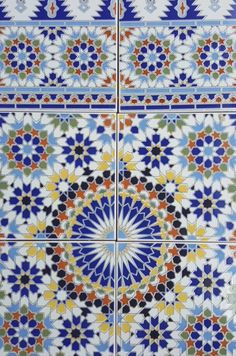 an artistic tile design in blue, green and orange colors with white flowers on it