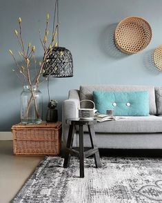 a living room with a gray couch, blue pillows and some plants in vases