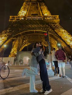 a man and woman kissing in front of the eiffel tower, at night