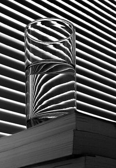 a glass sitting on top of a stack of books next to a window covered in blinds