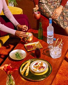 two women are sitting at a table with food and drinks on it while another woman holds a drink in her hand