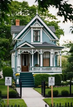 a blue house with white trim on the front porch and green shutters, surrounded by greenery