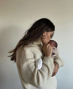 a woman holding a baby in her arms while wearing a white sweater and earrings