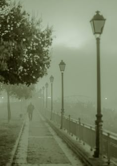 a man walking down a sidewalk next to a lamp post on a foggy day