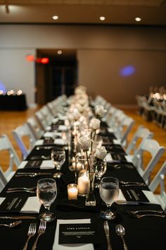 the long table is set with black and white linens, silverware, and candles