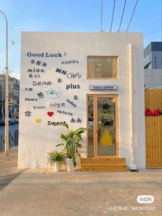 a small white building with writing on the side and plants in pots next to it