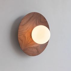 a wooden wall light with a white ball on it's side, against a gray background