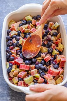 someone spooning blueberries and apples into a casserole dish with a wooden spoon