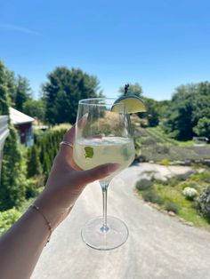 a person holding up a wine glass with a lemon wedge in it on the side of a road