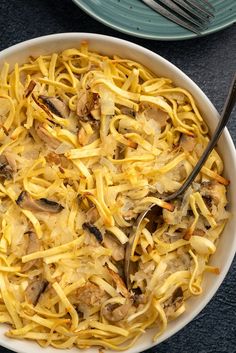 a white bowl filled with pasta and meat on top of a blue plate next to a fork