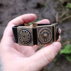 a person is holding two bracelets in their hand, one has a gold and black design on it