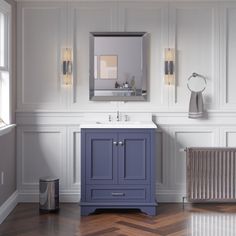 a bathroom with white walls and wood flooring has a blue cabinet, mirror and radiator