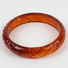 This is a lovely red tea amber Bakelite carved bracelet bangle. It features a spacer domed shape with deep geometric carving all around. The color is an intense red-amber tone with complete translucency.  Measurements: Inside across is 2.63 in diameter (6.7 cm) - outside across is 3.19 in diameter (8.1 cm) - width is 0.63 in wide (1.5 cm) - The inner circumference of the bracelet is 8.28 in (21.04 cm).  Please see the measurements noted above in the description for the best approximate dimension Elegant Orange Bangle Bracelet, Elegant Round Carnelian Bracelets, Elegant Bakelite Bangle As Gift, Elegant Bakelite Bangle As A Gift, Formal Brown Round Bangle, Brown Bakelite Bangle Bracelet, Elegant Bakelite Bracelet Jewelry, Elegant Bakelite Bracelet, Intaglio Bangle Bracelets As A Gift